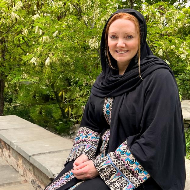 Woman in black abaya sitting outdoors.