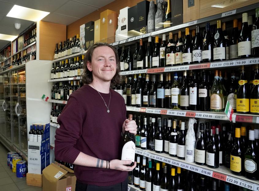 A man stands in a wine shop, holding a bottle of wine.