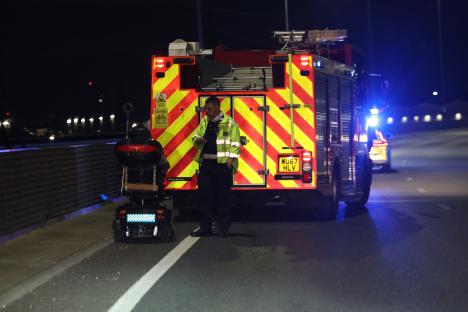 Police officer assisting a man on a mobility scooter on a highway at night.