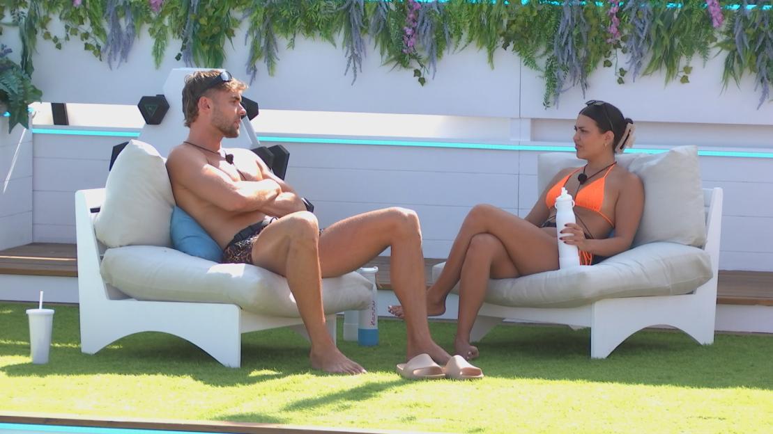 A man and a woman sitting on outdoor chairs, talking.