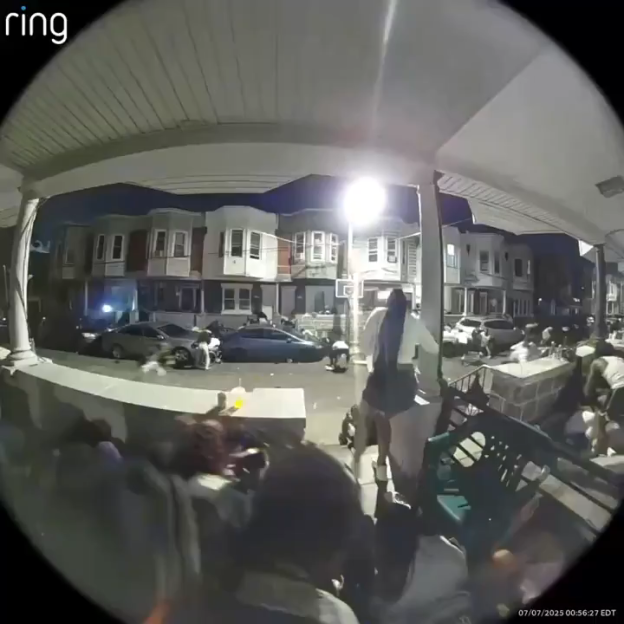 Nighttime security camera footage of a chaotic street scene with many people running.