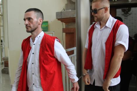 Two handcuffed men in red vests and white shirts.
