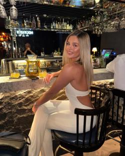 Woman in white outfit sitting at a bar.