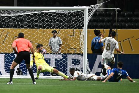 A soccer player scoring a goal despite the opposing goalkeeper's attempt to block it.