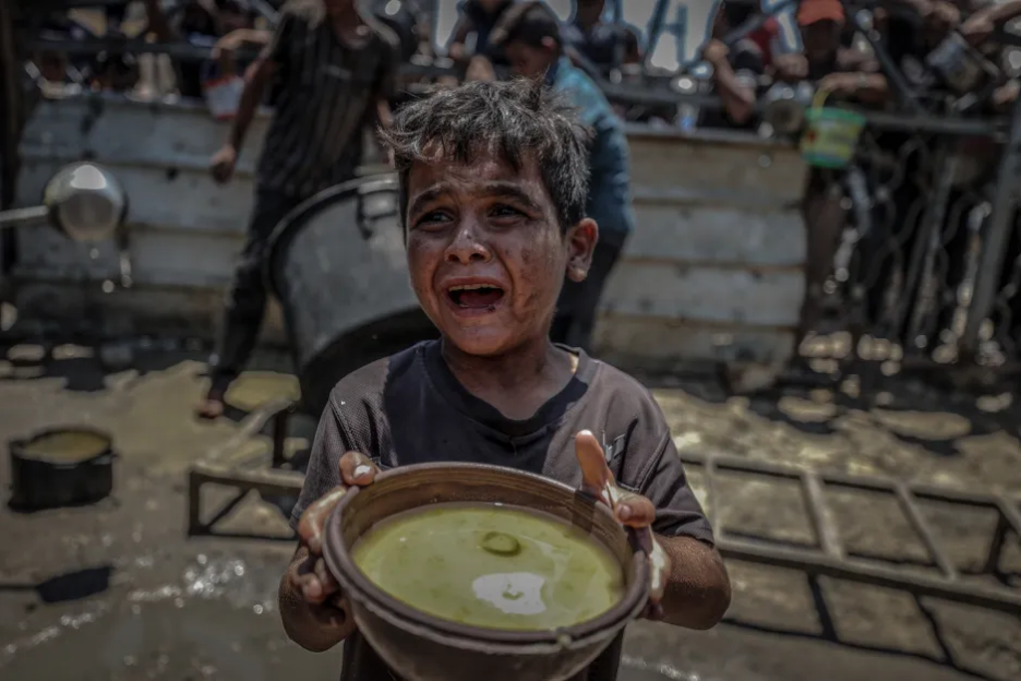 A dirty child cries while holding a bowl of food.