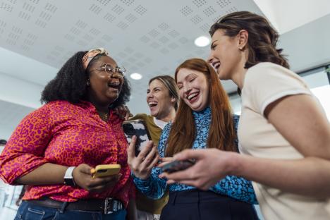 Four women laughing together and looking at their phones.