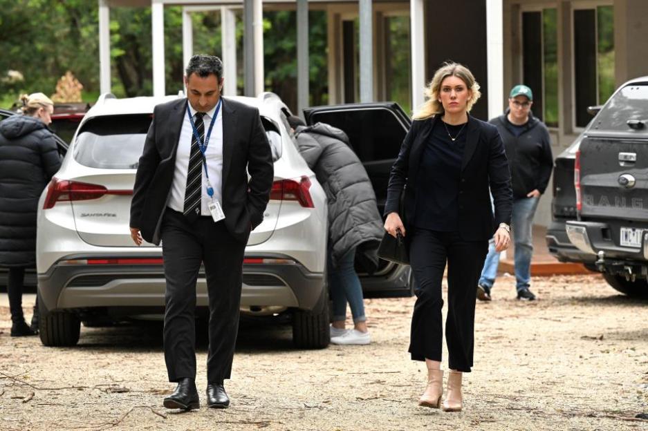 A man in a suit and a woman in a blazer walking away from a car.