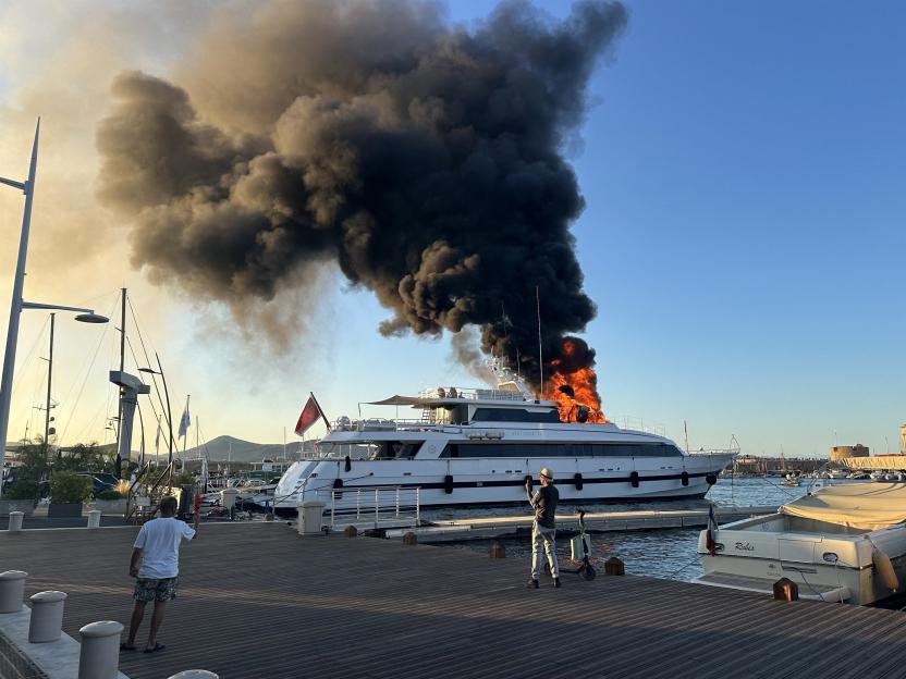 A large yacht on fire in a harbor.