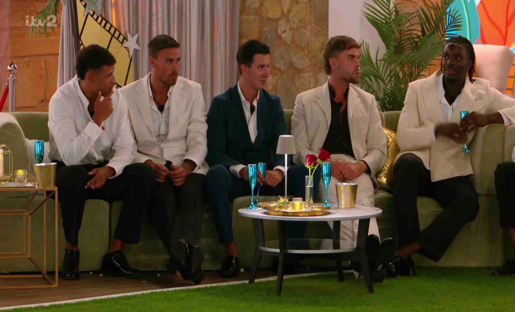 Five men in white jackets seated on a couch at a party.