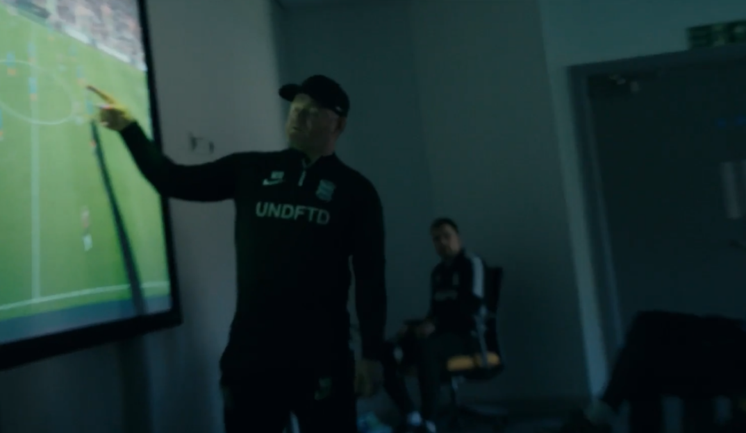 A coach points at a soccer strategy displayed on a screen.
