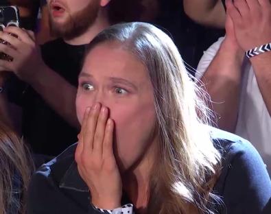 Ronda Rousey with a shocked expression, covering her mouth with her hand.