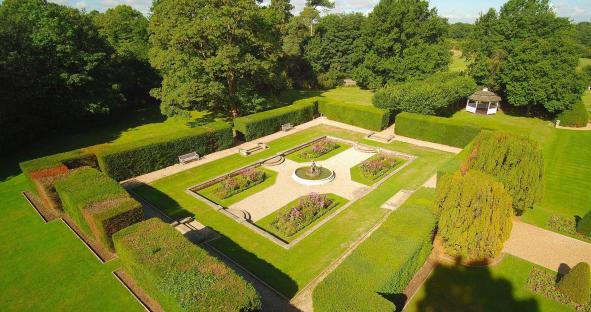 Aerial view of a formal garden with hedges, flowerbeds, a fountain, and a gazebo.