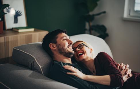 A smiling couple cuddling on a couch.