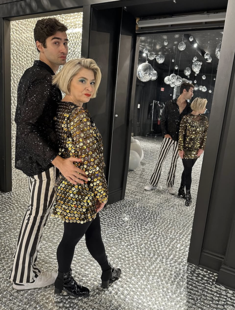 Couple in sparkling attire standing in a mirrored room.