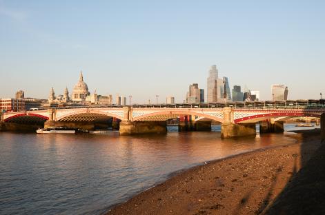 Blackfriars Bridge over the River Thames in London, with St. Paul's Cathedral and the city skyline in the background.