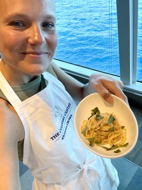 Woman in an apron holding a bowl of pasta.