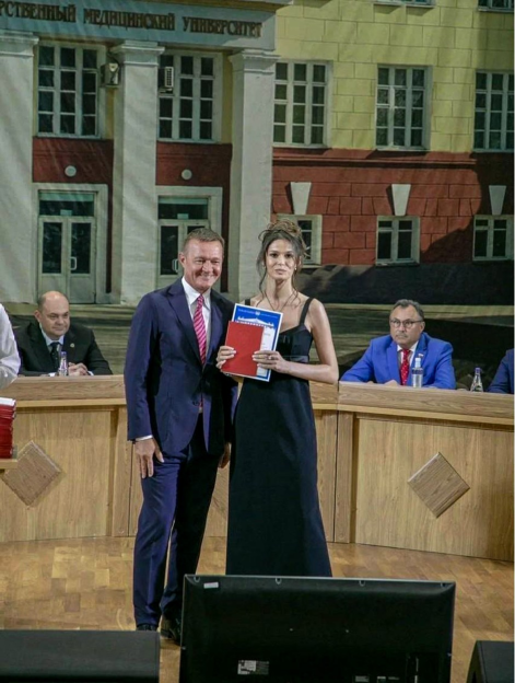 Woman in a black dress receiving an award from a man in a suit.