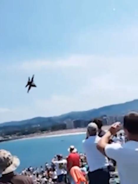 Jet flying low over beach crowd.