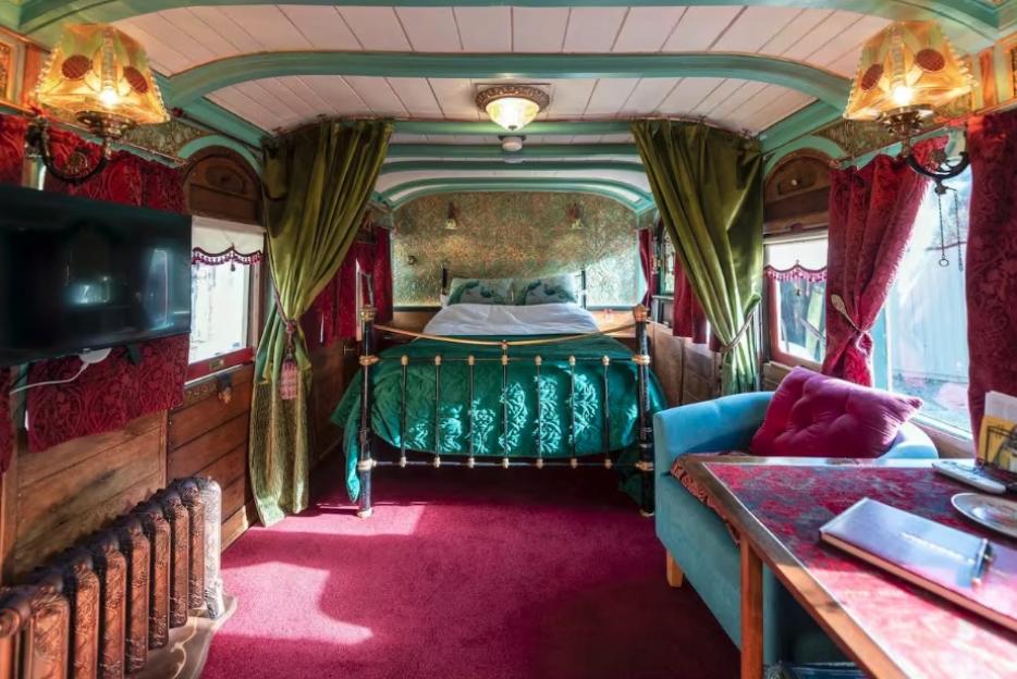 Interior of a restored 1895 GWR railway carriage, showing a bed, seating area, and small table.