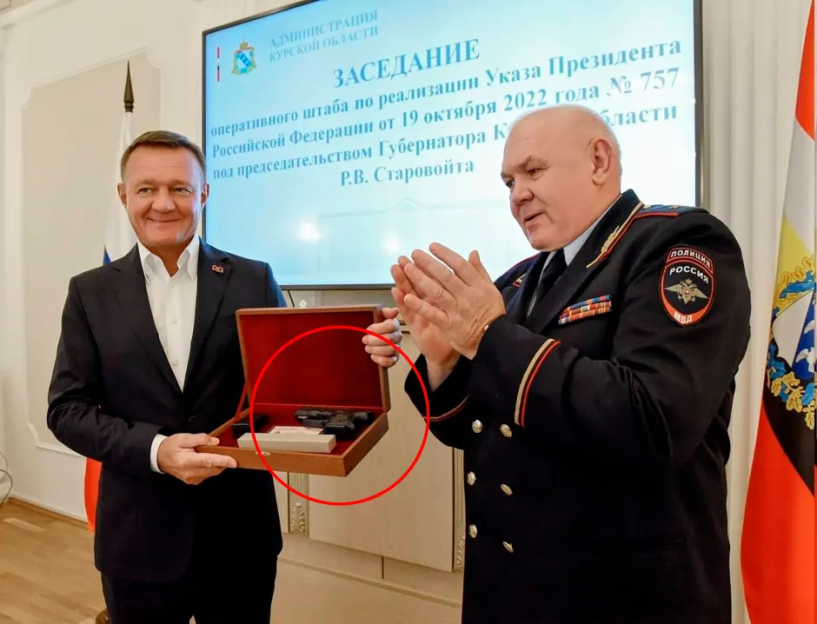 Man in suit presenting a wooden box to a man in uniform.