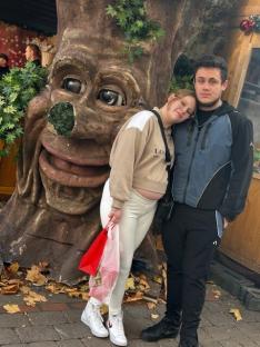 Pregnant woman and man posing by a whimsical tree sculpture.