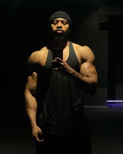 Man taking a selfie in a dark gym, showcasing his muscular physique.