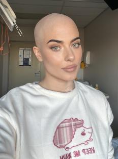 Woman with shaved head in hospital, wearing a white sweatshirt.