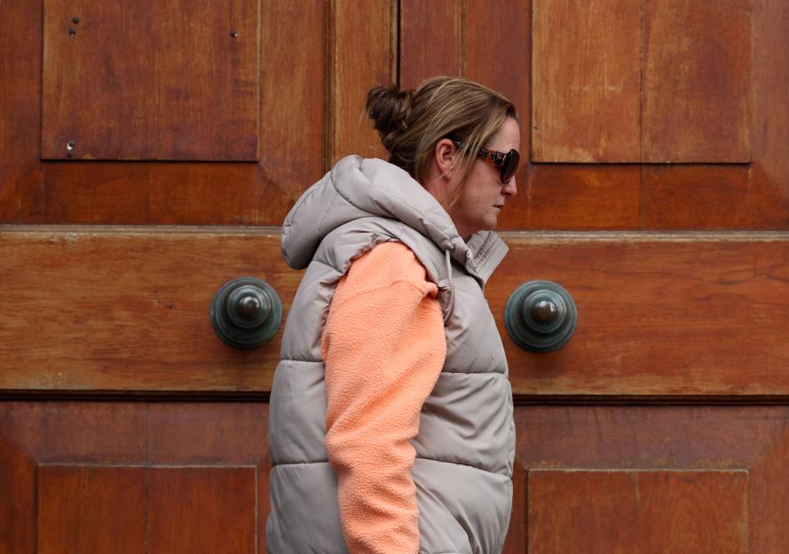 Woman wearing sunglasses and a puffer vest leaving a courthouse.