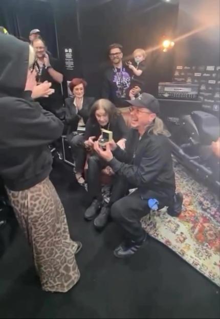 A man proposing to a woman surrounded by friends and family.