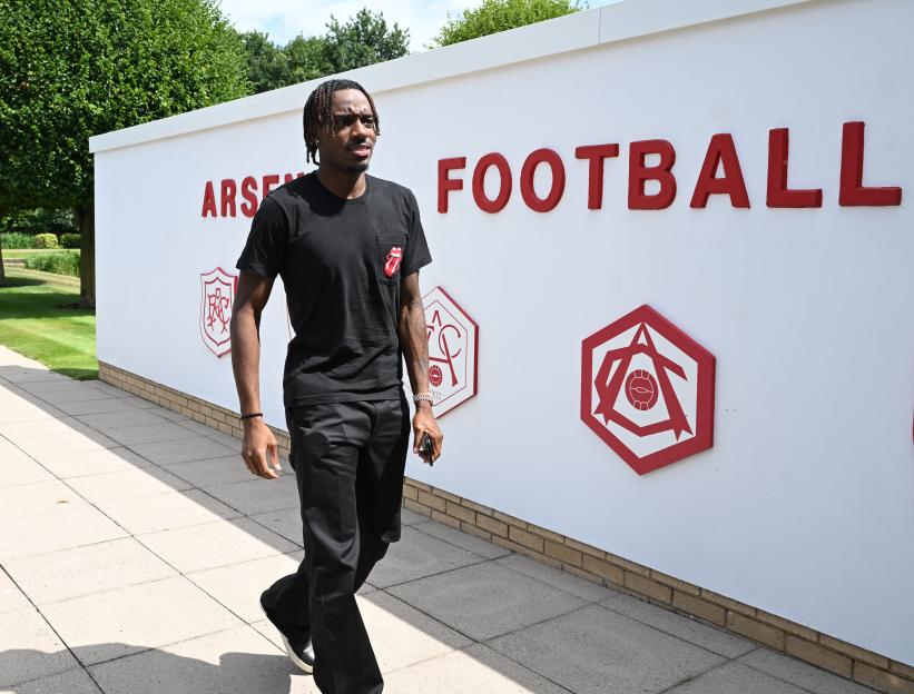 Noni Madueke walking past an Arsenal Football Club sign.