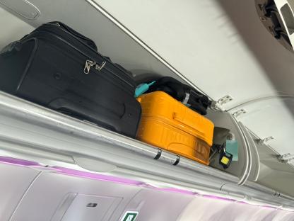 Stock photo showing close-up view of row of carryon luggage stored in overhead baggage compartments in an airplane cabin.