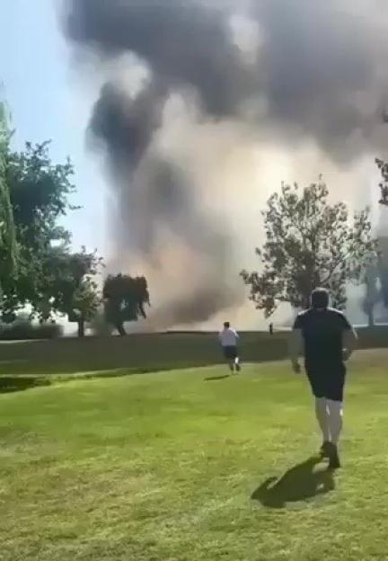 People running away from large plume of smoke rising in the distance.