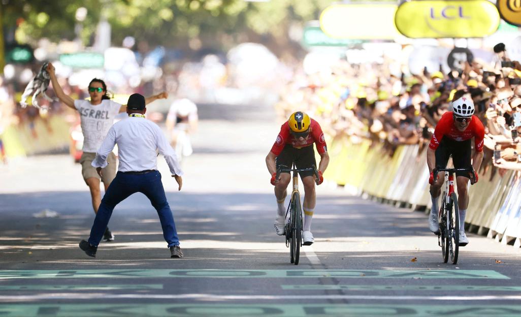 A protester runs onto a cycling race course wearing a shirt that says