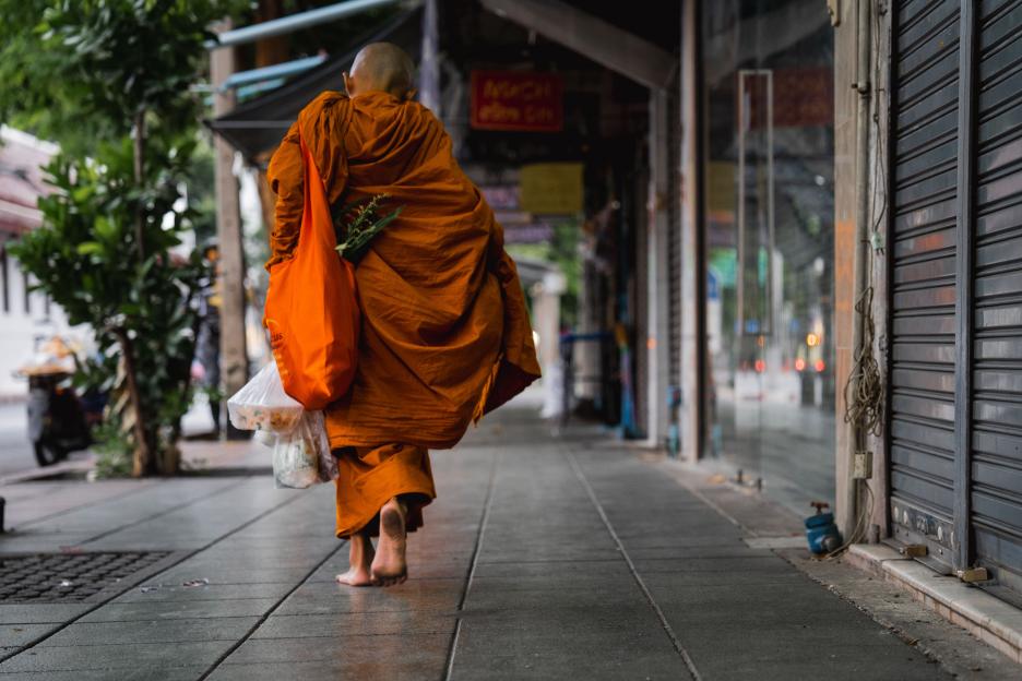 A Buddhist monk walks barefoot along a street carrying alms.