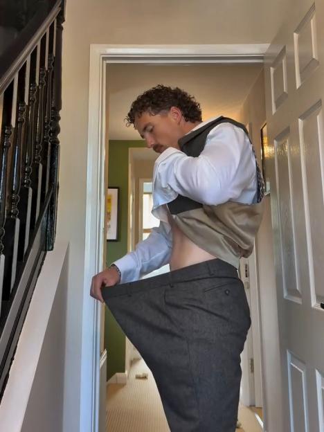 Man holding up a pair of significantly oversized trousers, showcasing his weight loss.