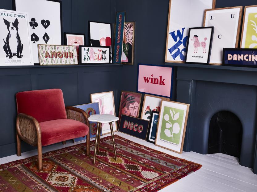 Room corner with red velvet armchair, patterned rug, and many framed prints on the wall and mantel.