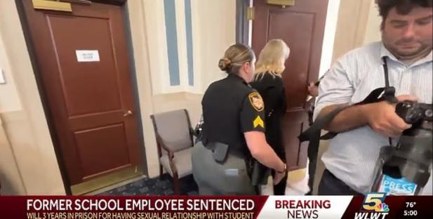 A female former school employee escorted by a police officer after being sentenced to three years in prison for a sexual relationship with a student.