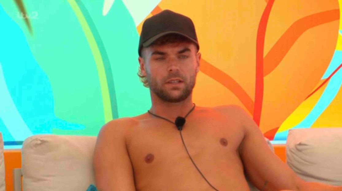 Harry from Love Island sits shirtless and speaks.