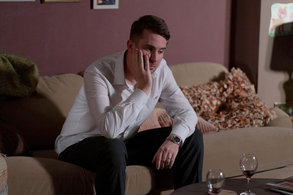 A man sits on a couch looking pensive.