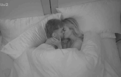 Couple kissing under covers in bed.