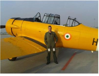 Man in flight suit standing next to yellow airplane.