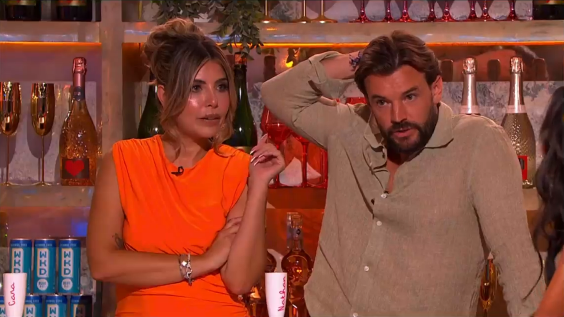 Woman in orange dress and man in tan shirt sitting at a bar.