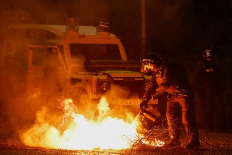 Riot police officer extinguishing a fire during a protest.