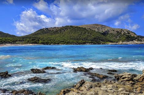 Cala Aguila beach in Mallorca, with turquoise water lapping rocks in the foreground.