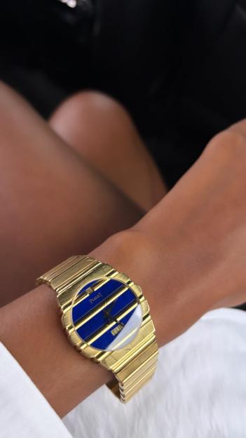 Gold Piaget watch with a blue face on a wrist.