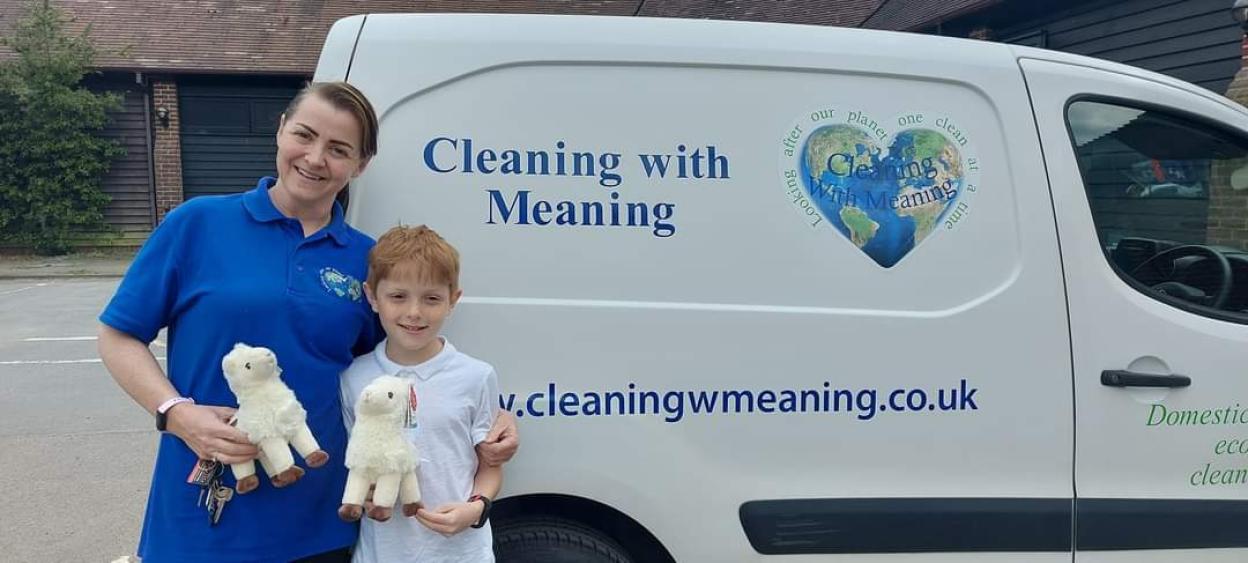 Woman and child with stuffed lambs in front of a Cleaning with Meaning van.