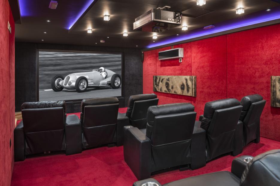 Home theater with red walls and black leather recliners.