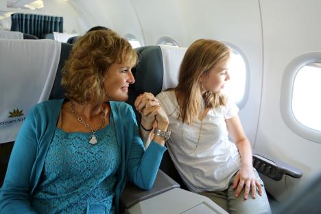 A woman and a girl hold hands on an airplane.