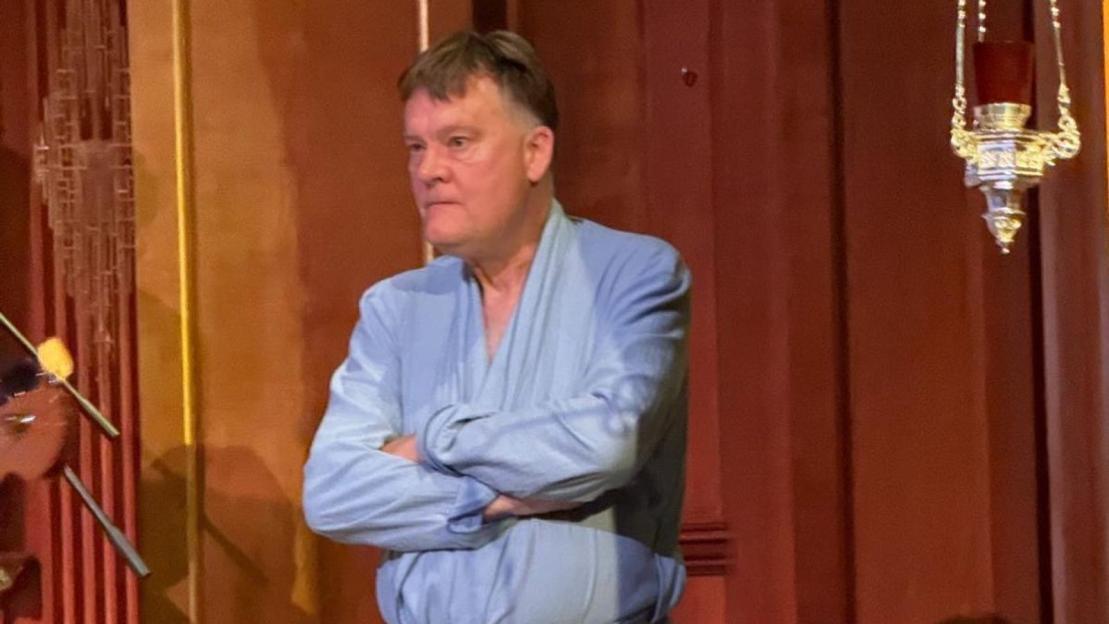 A man in a dressing gown asks a crowd to leave.