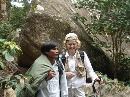 A man and woman hiking near a large rock.